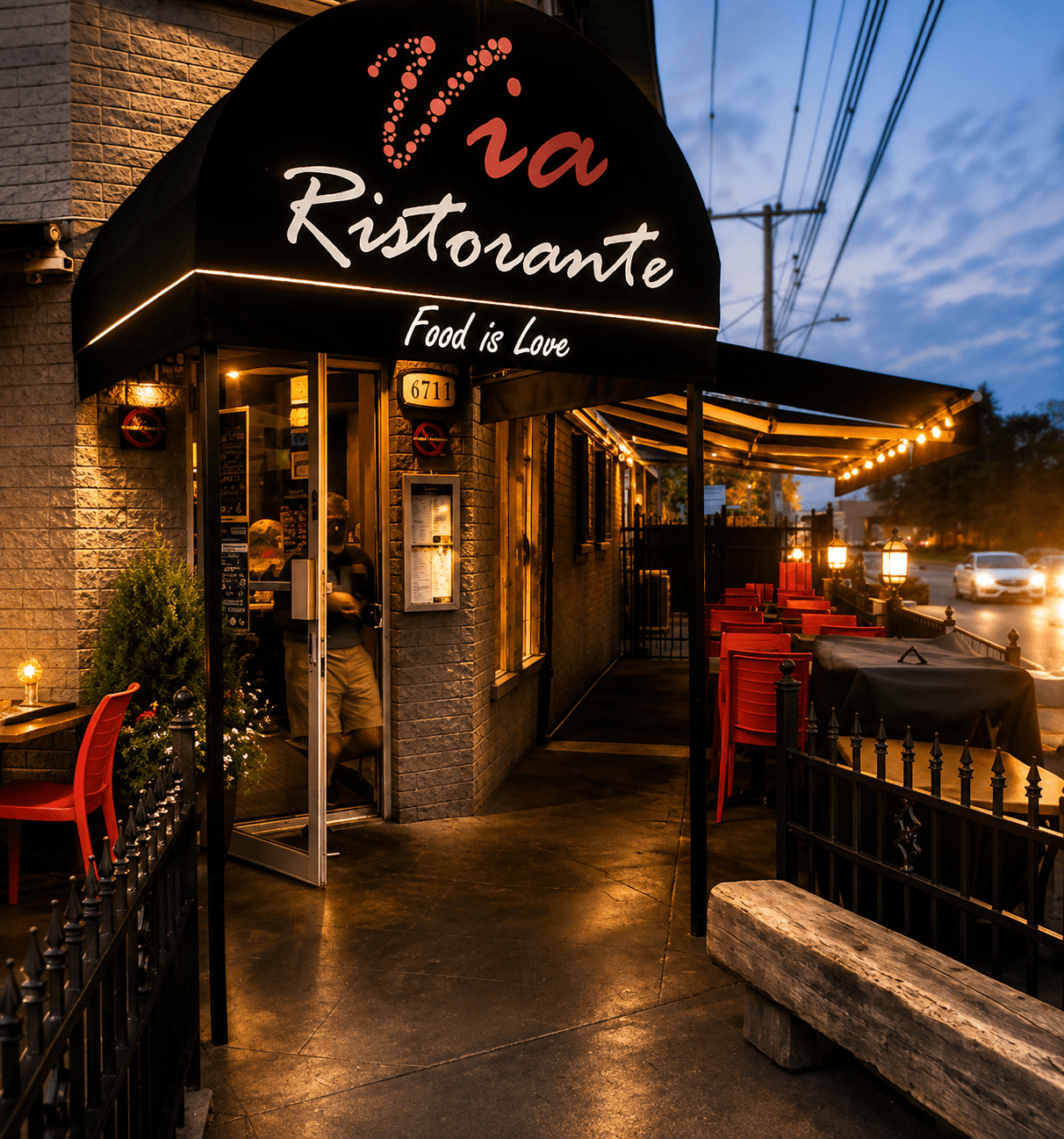 Entrée extérieure de Via Ristorante, avec son auvent illuminé et sa terrasse en soirée